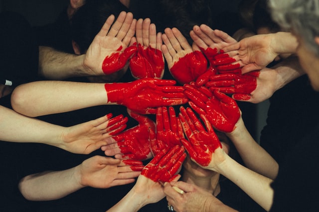 multiple hands together and overlapping, with a heart painted over the whole